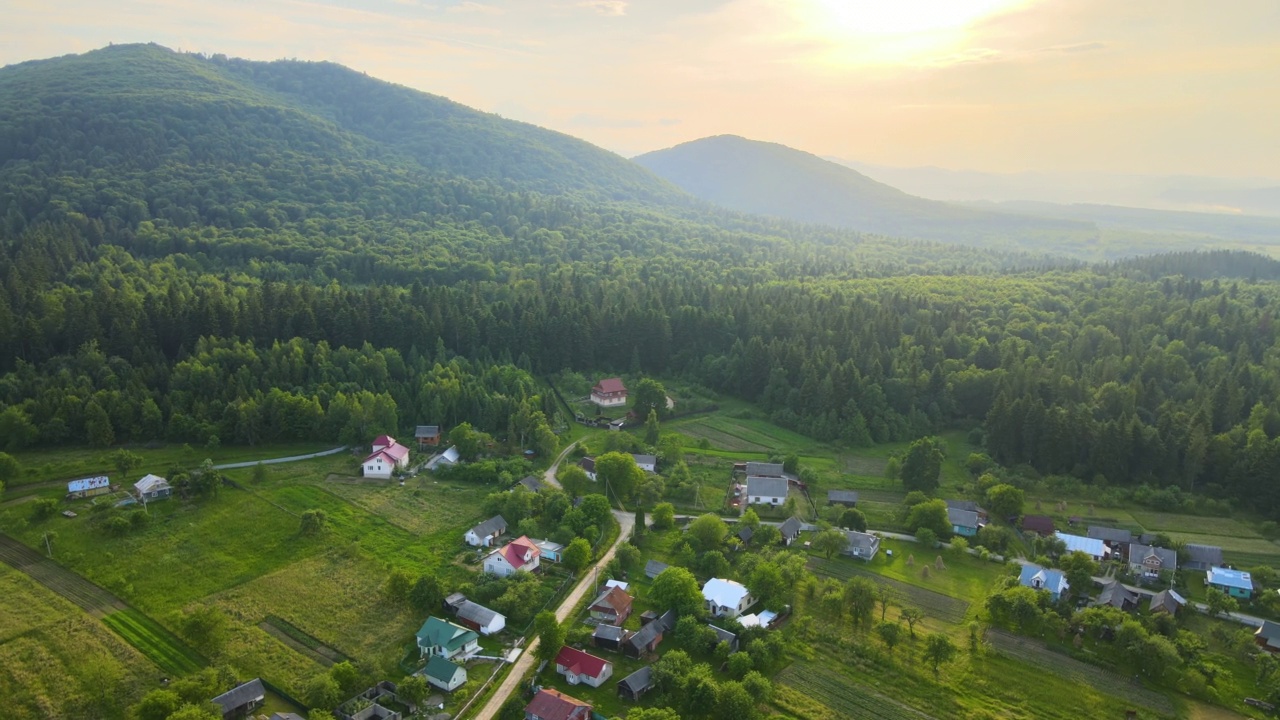 鸟瞰明亮雾蒙蒙的早晨在小乡村房屋之间的黑色山峰与山林树木在秋天日出。黎明时分的野生林地美景视频素材