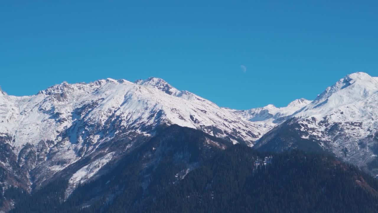 从印度喜马偕尔邦的马纳里，可以看到白雪覆盖的喜马拉雅山脉上的月亮。月亮从白雪皑皑的山峰上升起。自然景观背景。视频素材