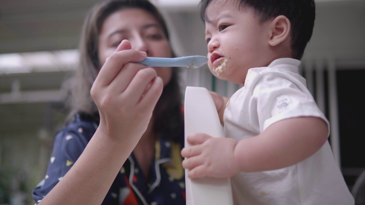 快乐的亚洲妈妈在家里给嘴巴沾满污渍的儿子喂食物。视频素材