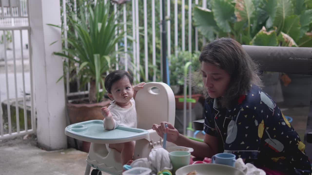 快乐的亚洲妈妈在家里给嘴巴沾满污渍的儿子喂食物。视频素材