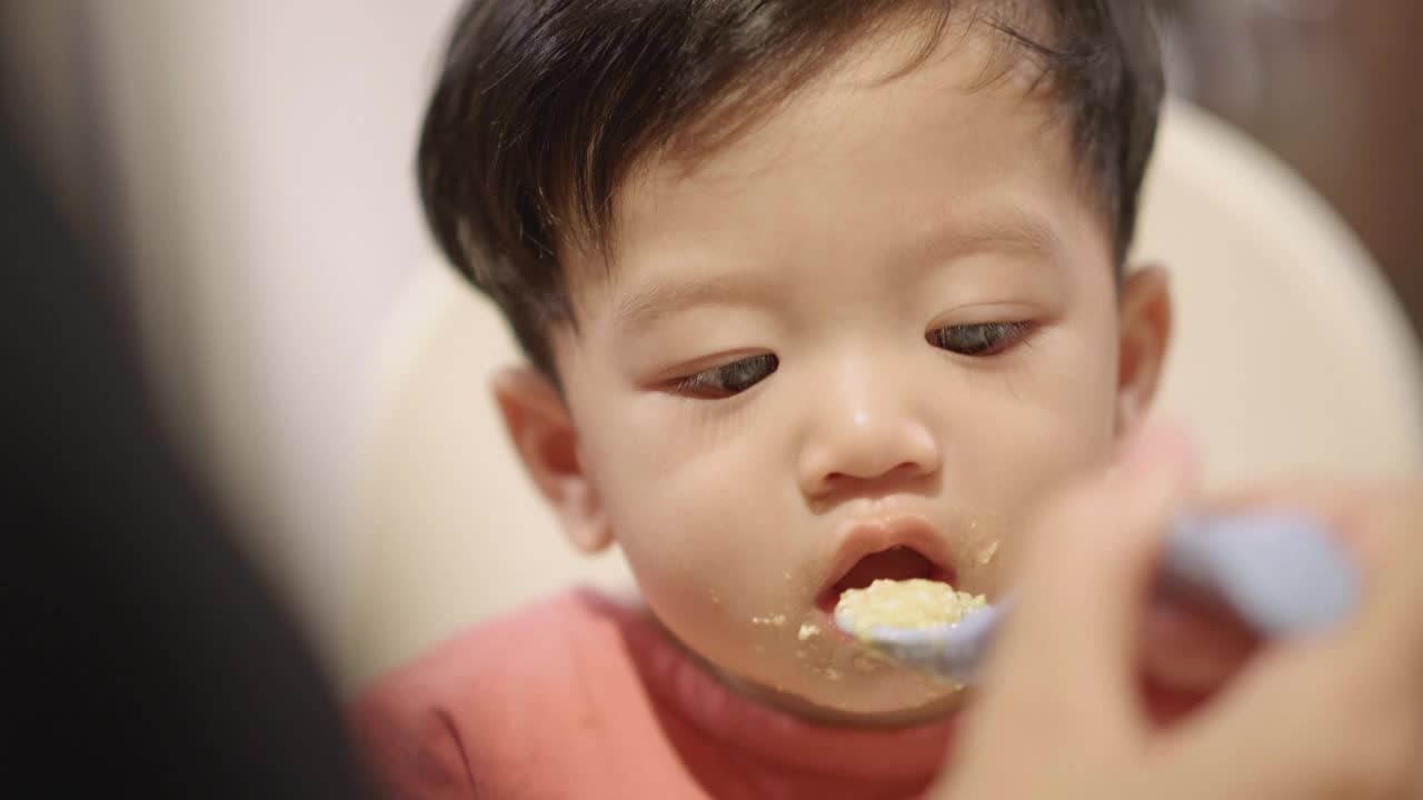 快乐的亚洲妈妈在家里给嘴巴沾满污渍的儿子喂食物。视频素材