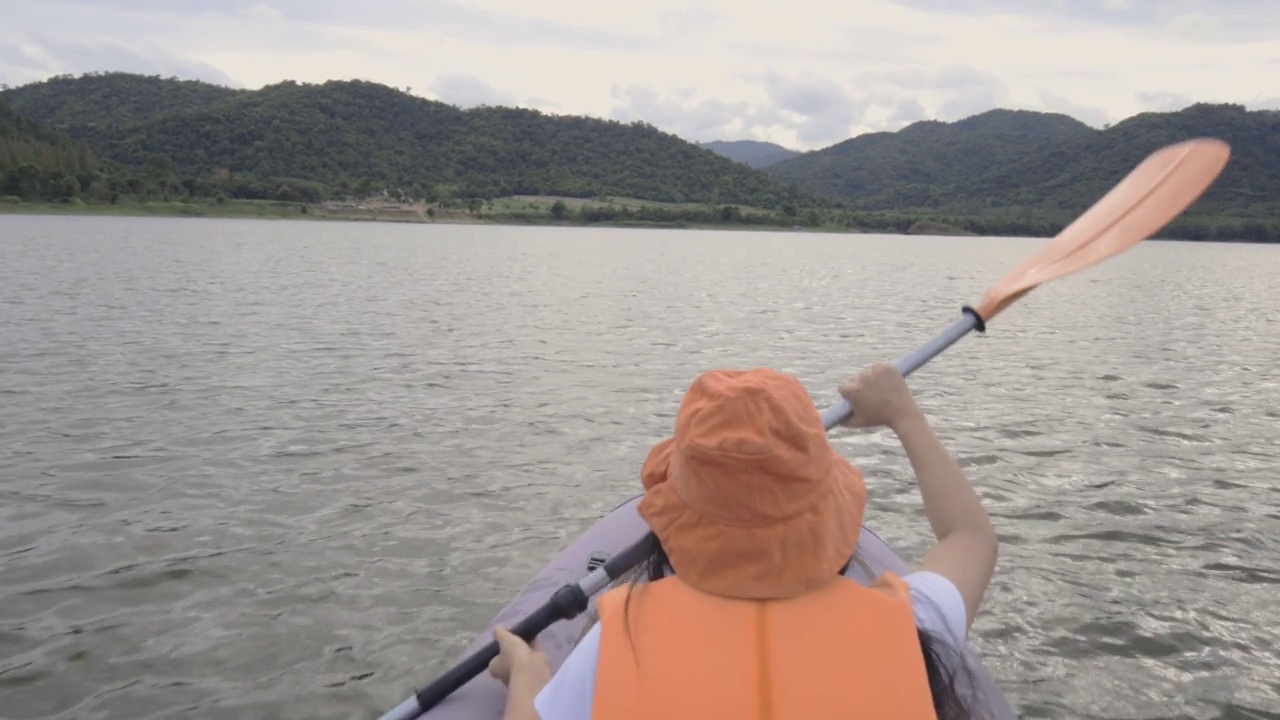 后景迷人的年轻女子划着充气皮艇在水的大山湖。旅游目的地，探险，度假度假的概念。视频素材