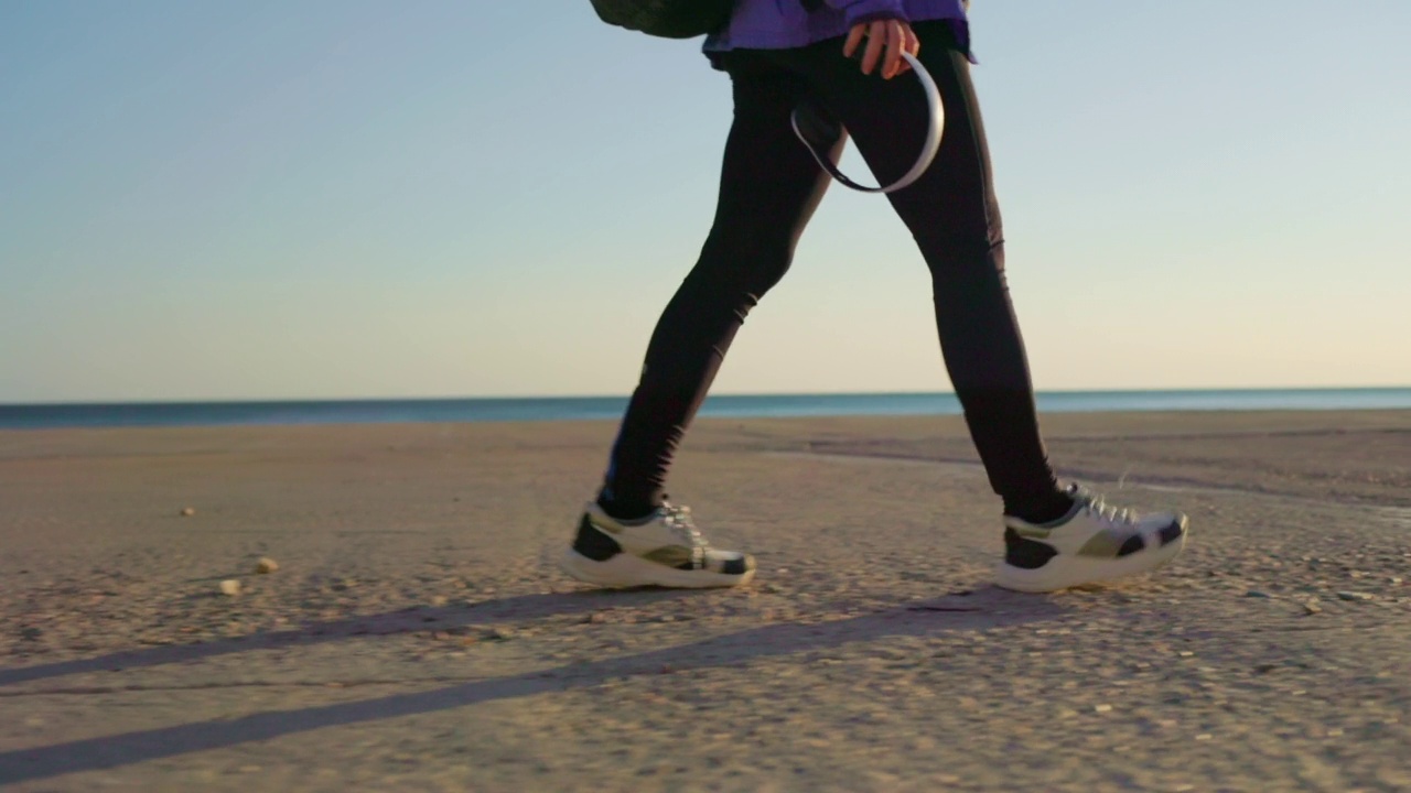 徒步旅行。一个穿着运动服的女人沿着海滩散步。侧视图，跟踪镜头，低角度视图。背景是地平线。副本的空间。自由和旅行的概念视频素材