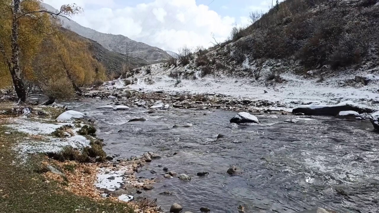 一条山间小河的两岸，覆盖着初雪的粉末，在一个风景如画的山谷中流淌。视频素材