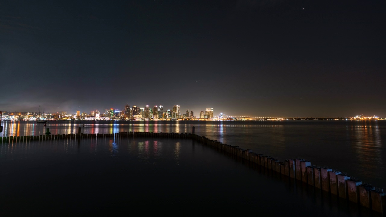 时光流逝的封锁拍摄的波光粼粼的大海在闪耀的现代城市在夜晚晴朗的天空-圣地亚哥，加利福尼亚州视频素材