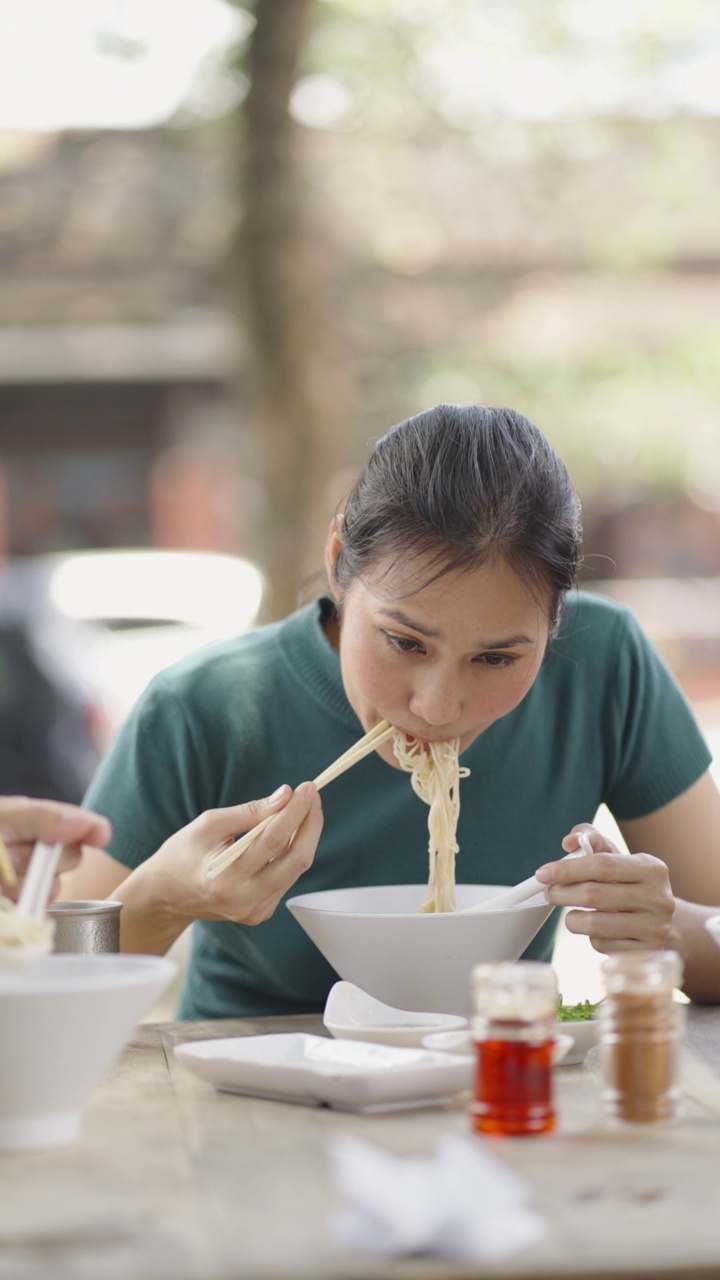 垂直-年轻美丽的亚洲女子吃拉面汤，户外街头餐厅视频素材