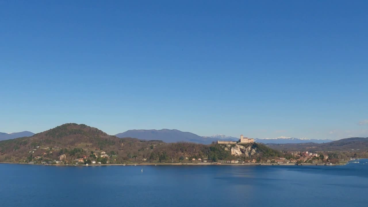 美丽的马乔雷湖和安杰拉要塞的全景，天空晴朗，小船在平静的水面上航行。缩小视频素材