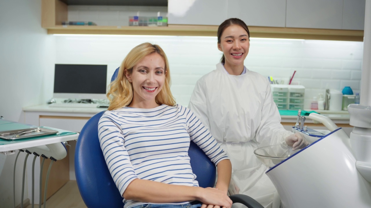 在保健诊所的白人妇女病人和牙医的肖像。迷人的女孩在约见医生时接受牙科治疗后坐在牙科椅上，然后看着镜头。视频素材