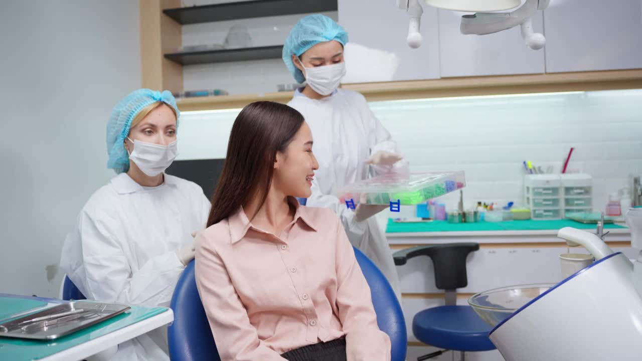 亚洲女性病人在诊所与正畸医生选择金属牙套。迷人的女孩带着牙套坐在牙科椅上，在医院的程序服务中接受牙医的牙科治疗。视频素材