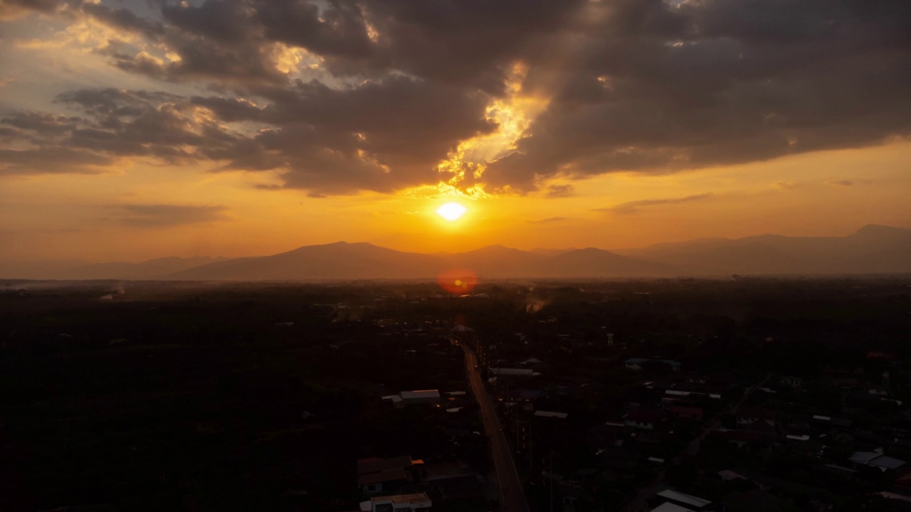 夕阳下的天空，金色的阳光映衬着山景和乡村的剪影。鸟瞰美丽的天空与云和阳光在日落时在乡村。视频素材