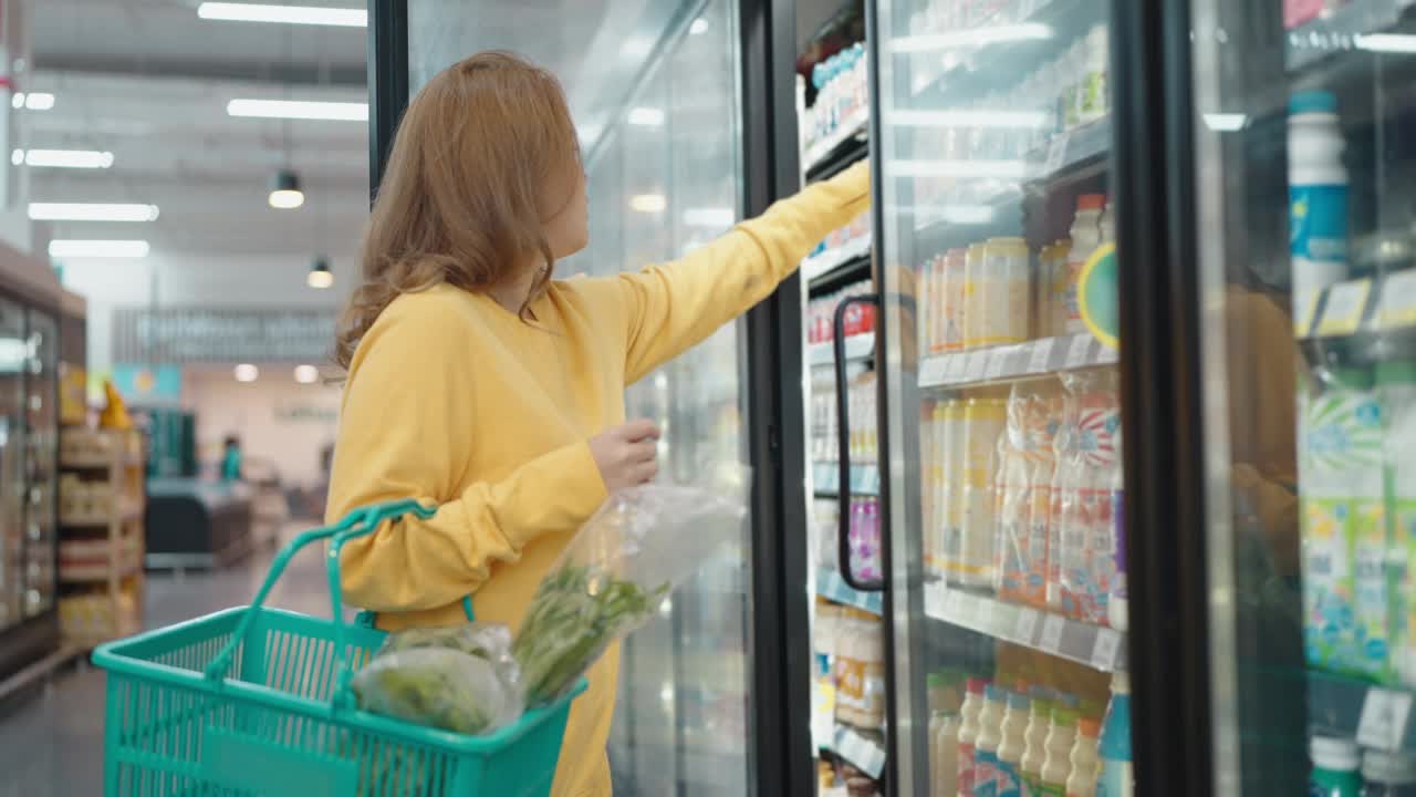 一位女士在冰箱的货架上购买食物并查看产品详情视频素材