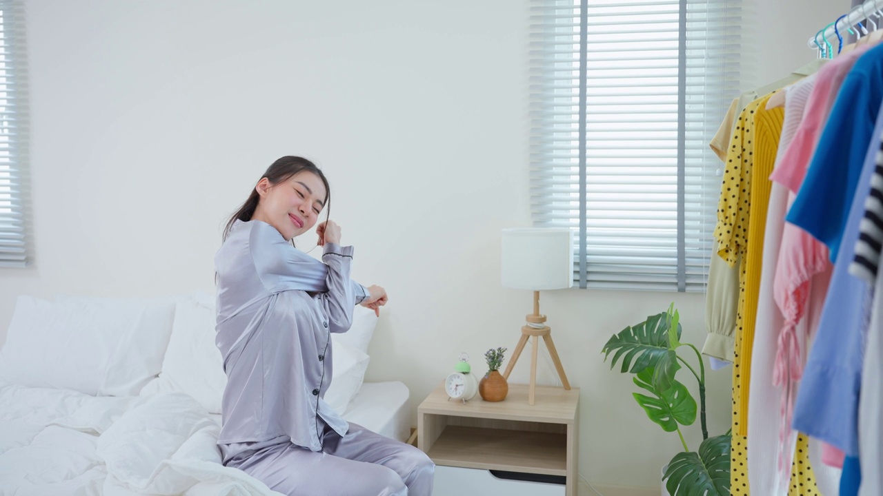 美丽的亚洲年轻女子在家里的衣柜架子上选择衣服。迷人的女性穿着睡衣感到快乐和放松，从床上醒来后在卧室的早上在家里换衣服视频素材