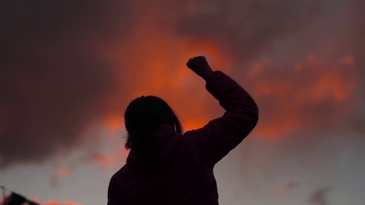 一个女孩在美丽的夕阳前举起手臂的剪影。成功的背景。女人在她的生活中取得了成功。视频素材