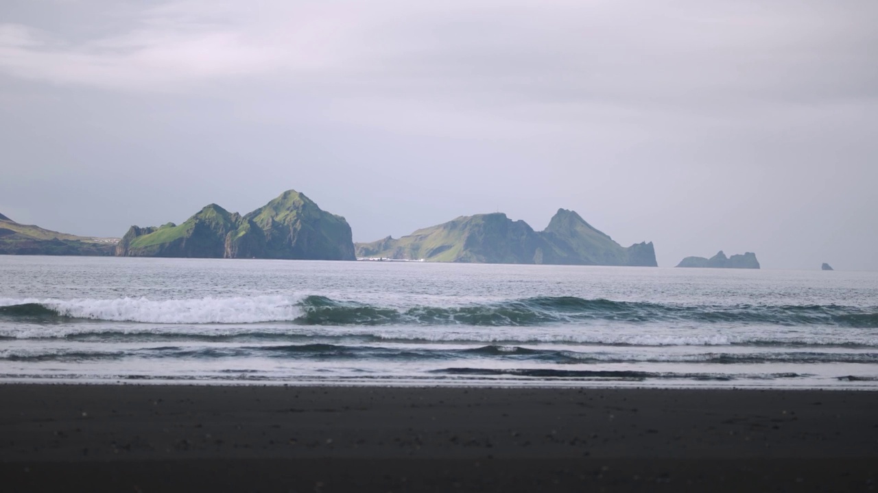 从沙滩上看，海浪撞向海岸，背景是岩石岛视频素材