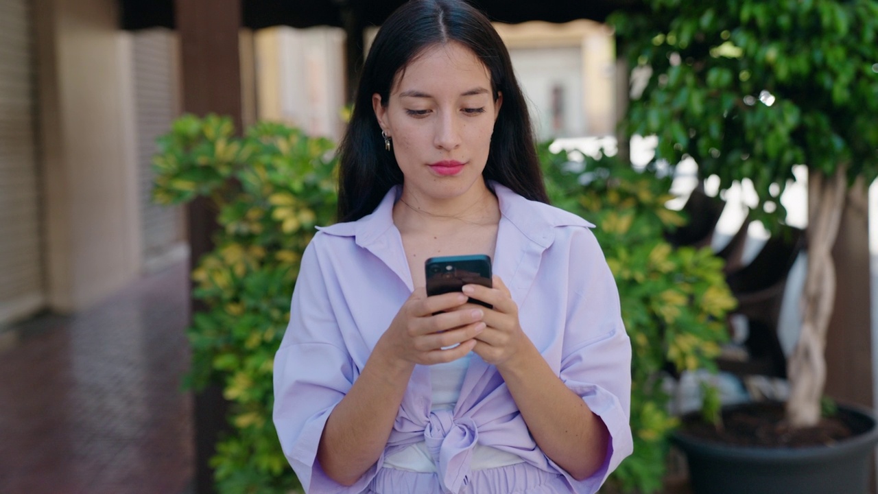 年轻美丽的西班牙妇女使用智能手机与严肃的表情在街上视频素材