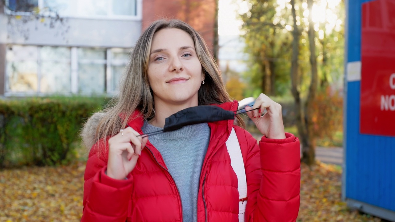 身穿红色衣服的快乐年轻女子摘下医用口罩，在新冠病毒检测台前看着你视频素材