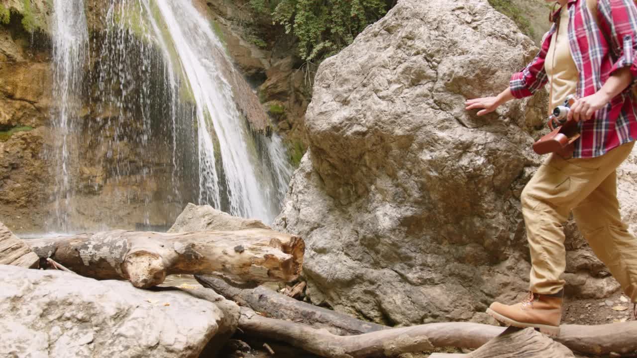 女摄影师旅行者世界探险家爬上山上的岩石捕捉美丽的瀑布照片视频素材