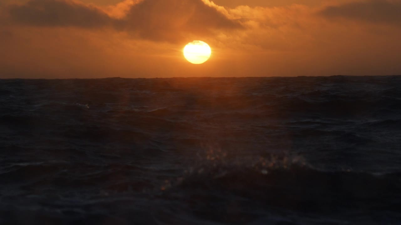 夕阳落在波涛汹涌的海面上，从一艘小船上驶过开阔的大海视频素材