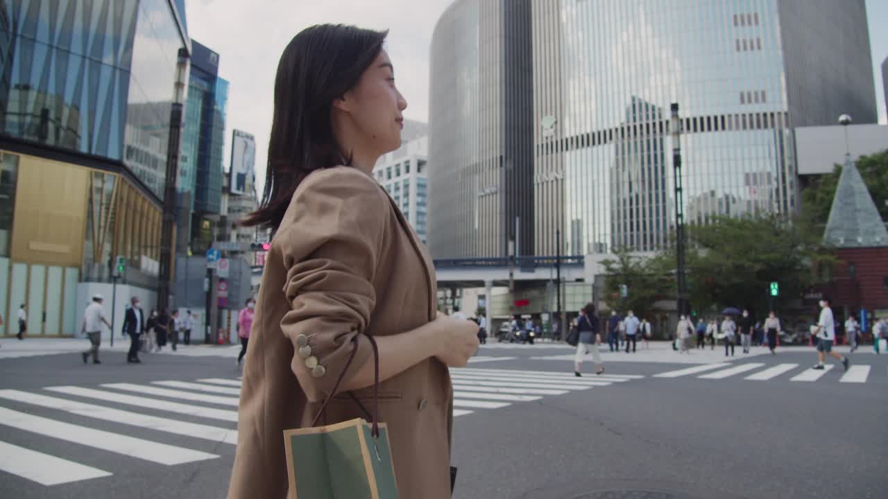 在东京购物。亚洲年轻女子带着购物袋走在斑马线上视频素材