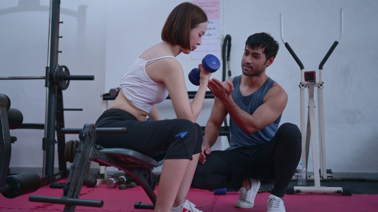 年轻夫妇在健身房锻炼举重时，他们互相帮助。视频素材