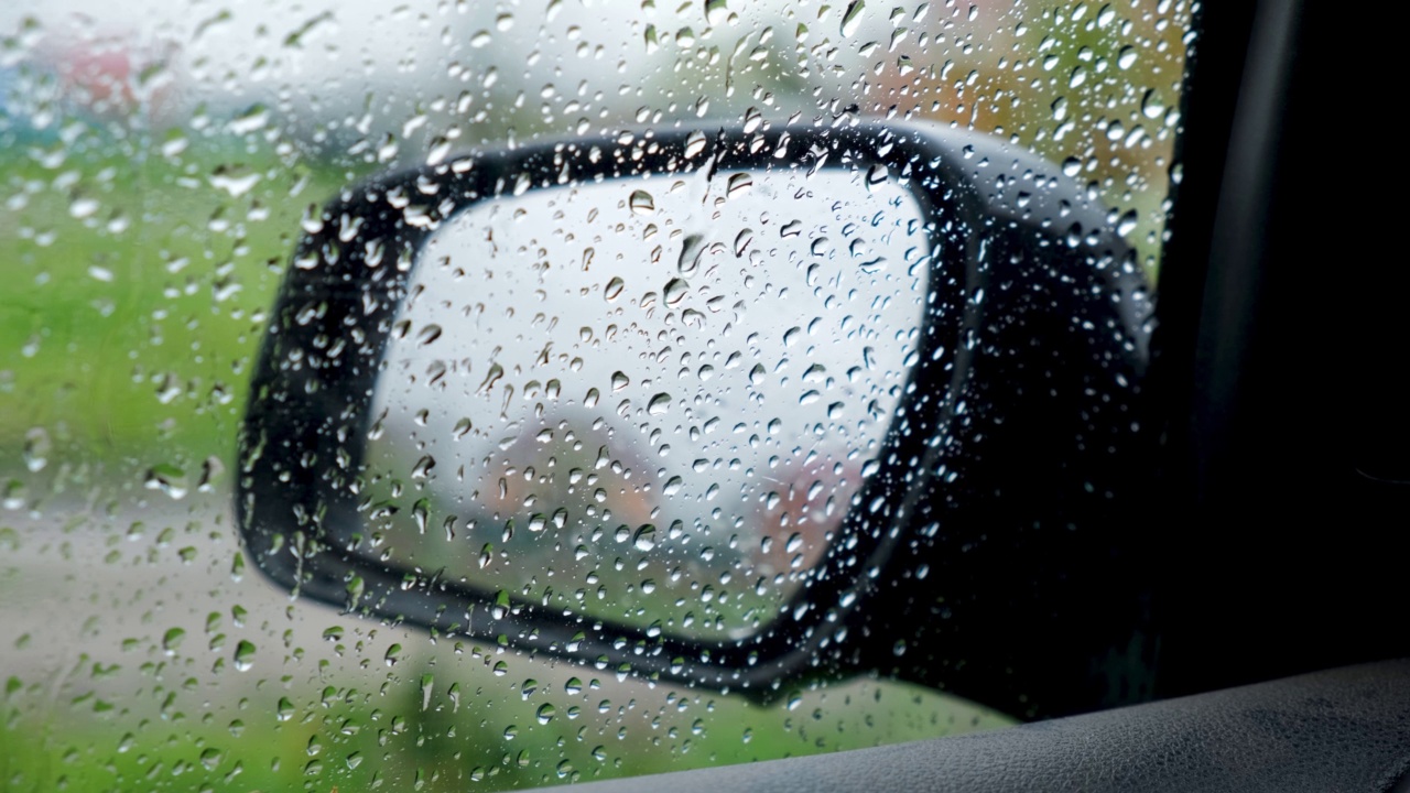 雨滴密切起来。从汽车内部的侧视镜与凝结和滴水的雨在窗户上。湿玻璃、降水。春天雨季。多云的一天。视频素材