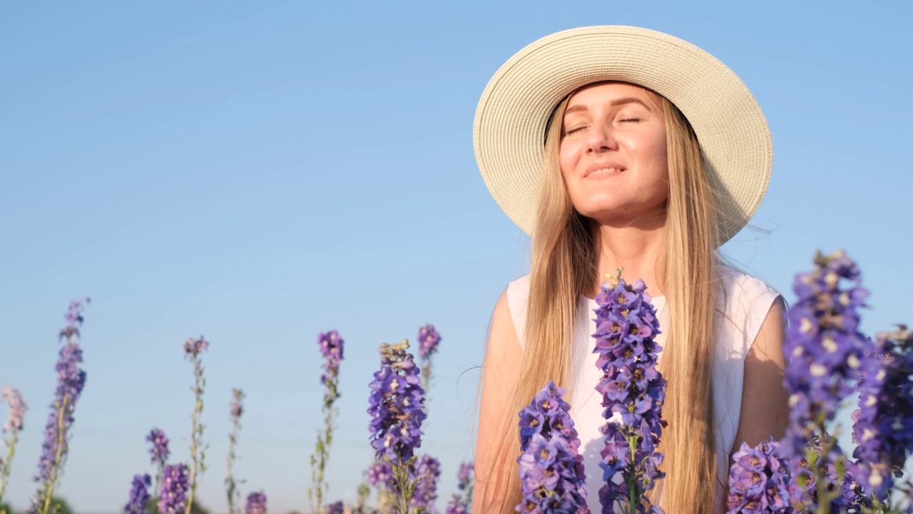 一位戴着白色帽子的欧洲模样的年轻女子在薰衣草田中间嗅着薰衣草花视频素材