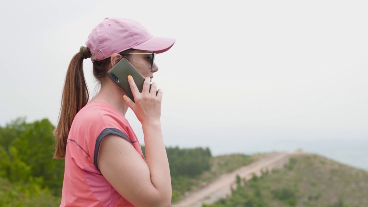 徒步女郎在大自然里打电话。坐在岩石上休息，欣赏美丽的风景。视频素材