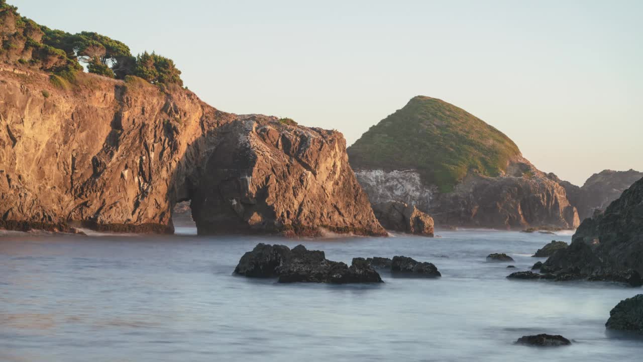 白天的海景平滑的海浪周围的岩石和一个海洞-时间推移视频下载