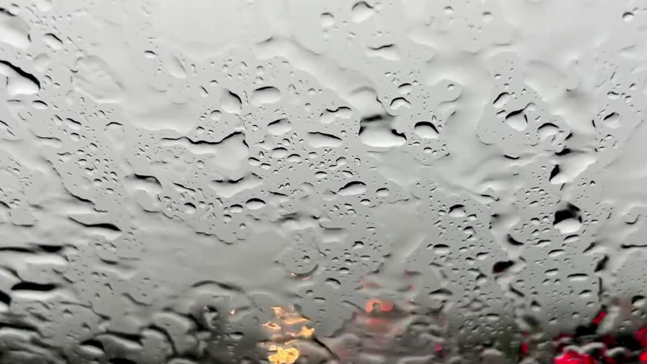 大雨落在挡风玻璃上，红色模糊了汽车交通的灯光背景，雨刷清理挡风玻璃上的雨滴视频素材