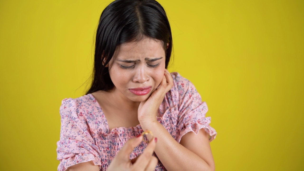 抑郁悲伤的年轻女子手里拿着戒指感觉心烦失望沮丧不快后悔错误遭受分手观念，孤立过黄背景视频素材