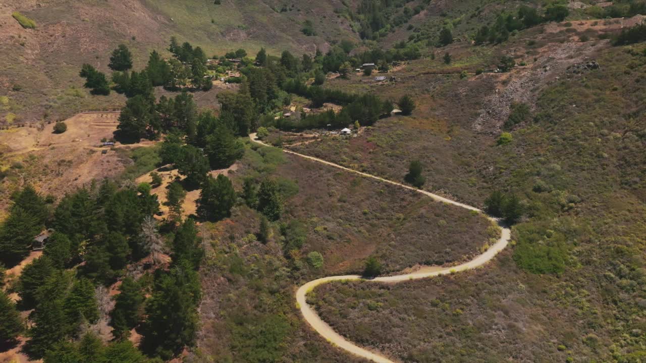 波浪形的道路穿过岩石景观，通向绿色枞树丛中的房屋。山在背景。前视图。视频素材