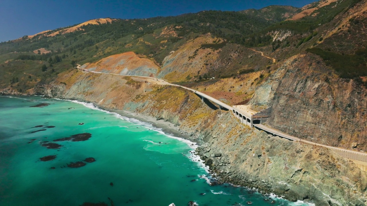 蓝绿色的海洋和冲击岩石的海浪，一派田园诗般的风景。穿过群山的公路。晴天的背景。视频素材