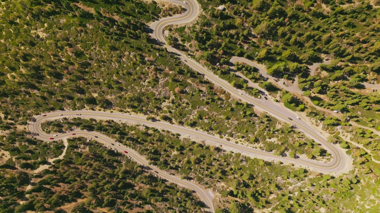 汽车在蜿蜒的道路上悠闲地行驶，穿过绿色的风景。无人机在阳光明媚的白天降落在高速公路上。视频素材