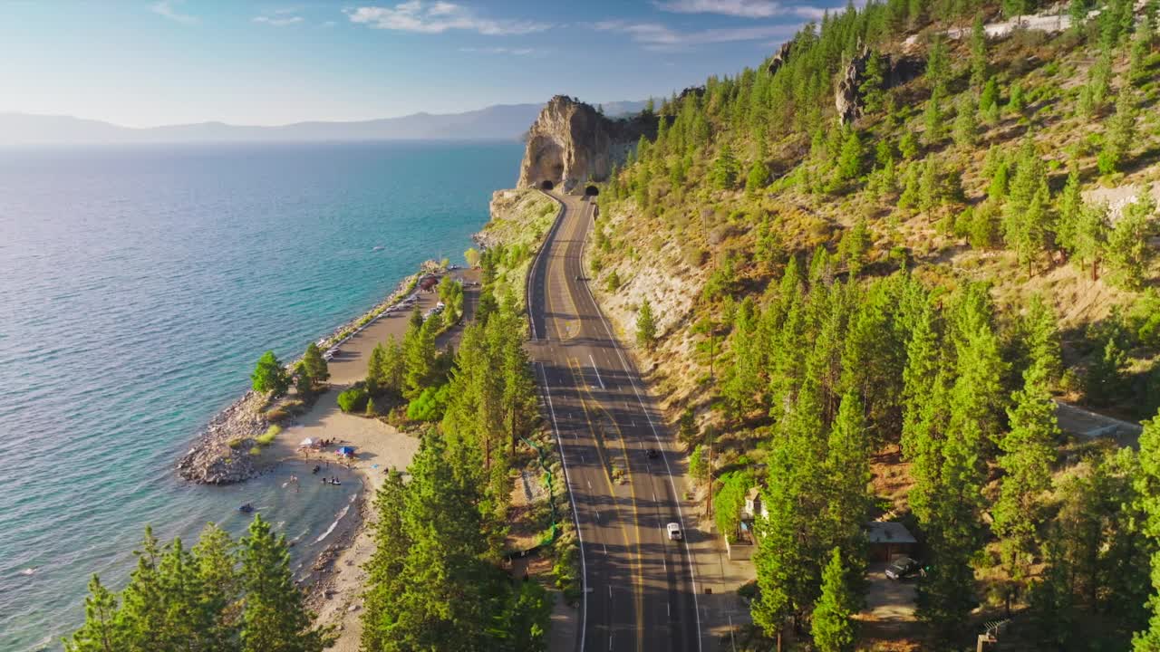 有隧道的高速公路穿山而过。岩岸，湖边有松树。蓝天为背景。视频素材