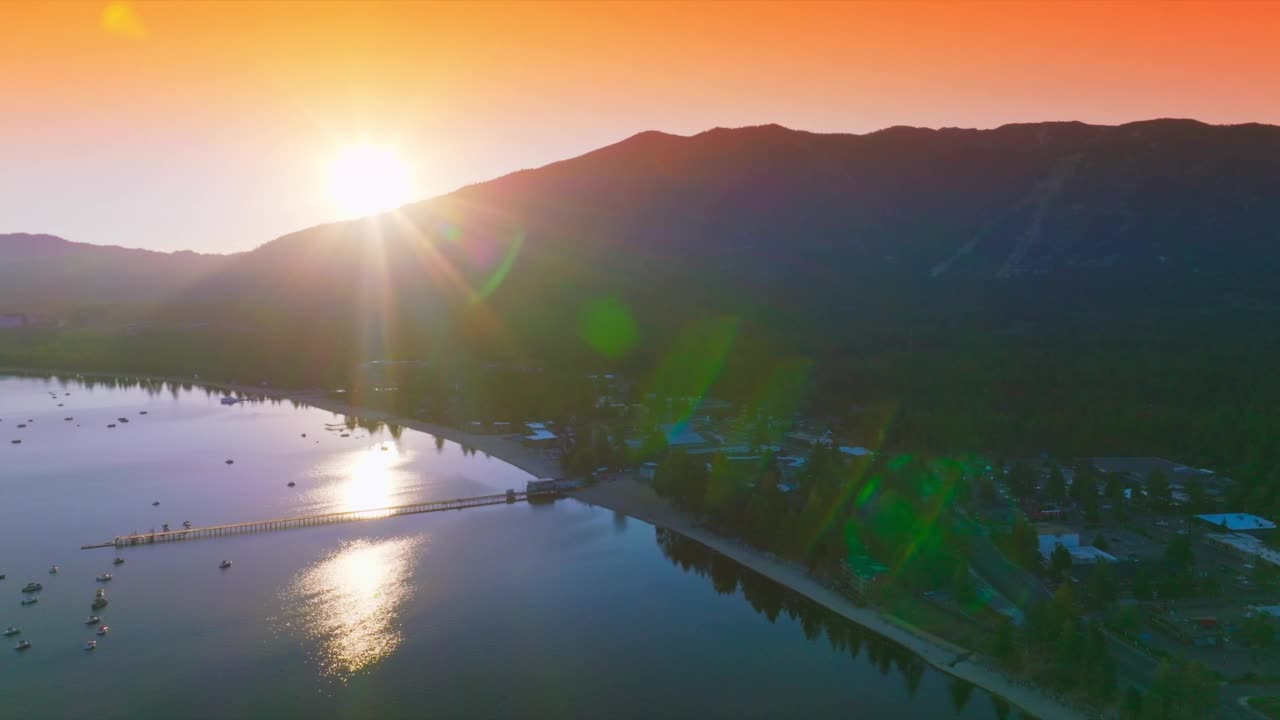 落日最后的余晖从高山后面照了出来。美丽的湖泊，岸边有城市基础设施。背景是橙色的天空。视频素材