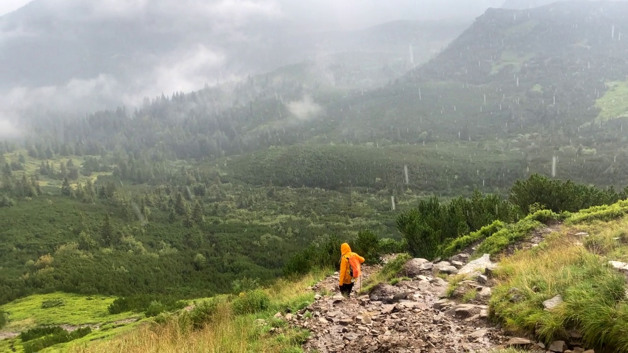 穿着黄色雨衣的女人在雨天沿着岩石小道走视频素材