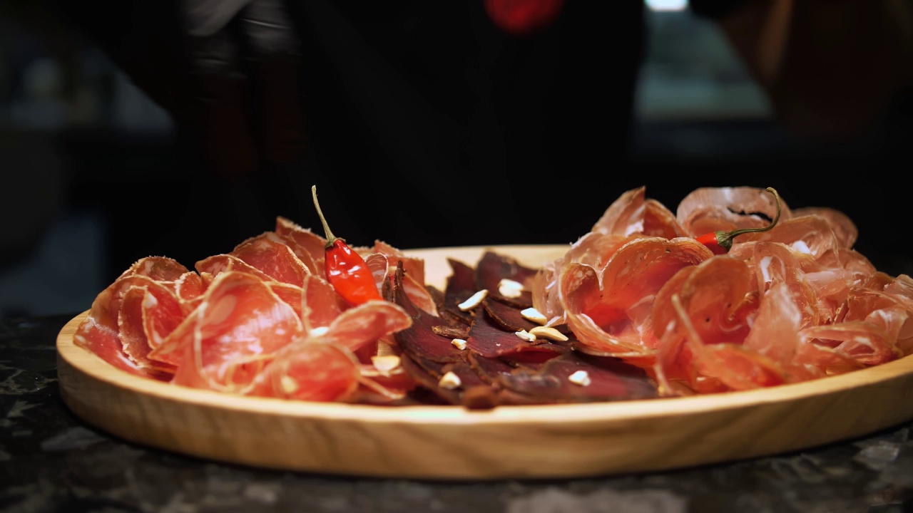 肉开胃菜。jamon。美味的各种肉类开胃菜，熏火腿或火腿肉与迷迭香服务木浅盘。厨师把火腿放在餐板上。视频素材