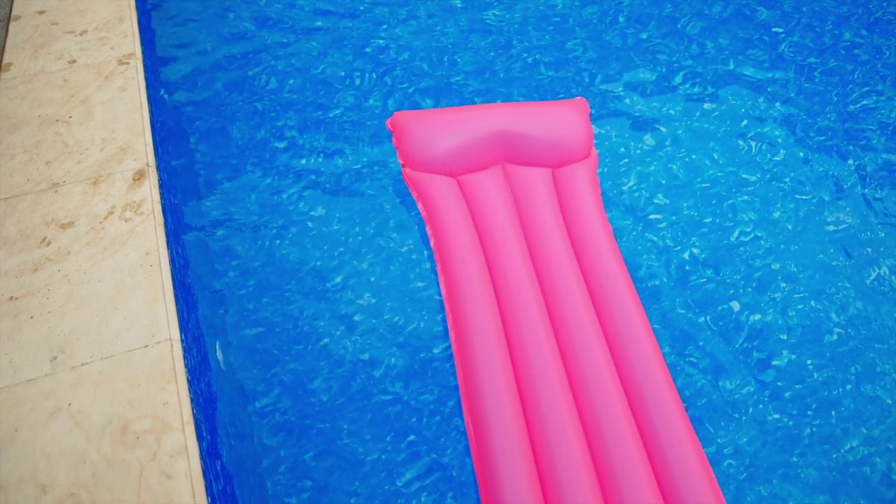 长长的粉色充气床垫在蓝色的水中。游泳池水边漂浮的床垫。视图从上。视频素材