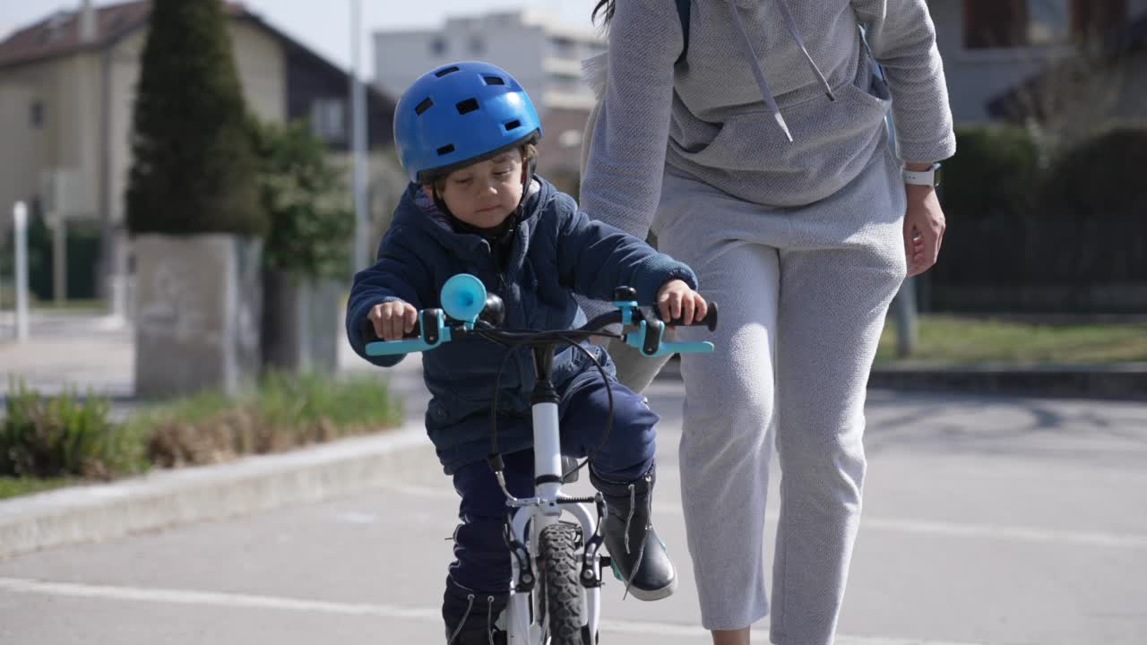 儿童在家长的帮助下在户外学习骑自行车。小男孩戴着头盔，穿着外套，在秋天骑自行车视频素材