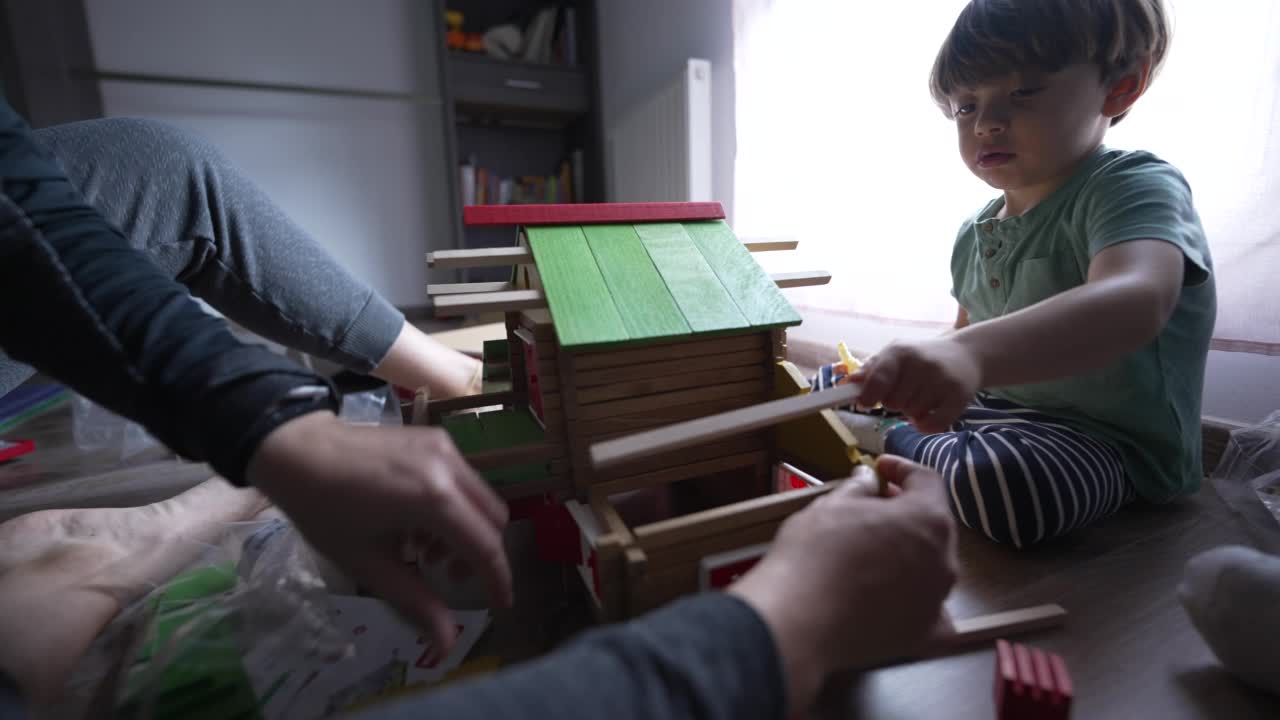 孩子和妈妈在房间里玩传统的木制家庭玩具。小男孩和父母一起盖房子视频素材