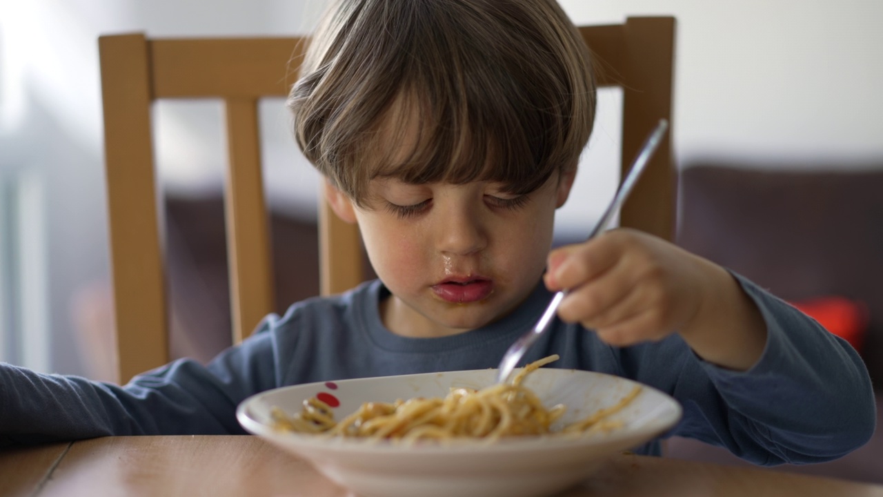 一个小男孩用叉子吃意大利面。孩子午餐吃碳水化合物食物。孩子营养的概念视频素材