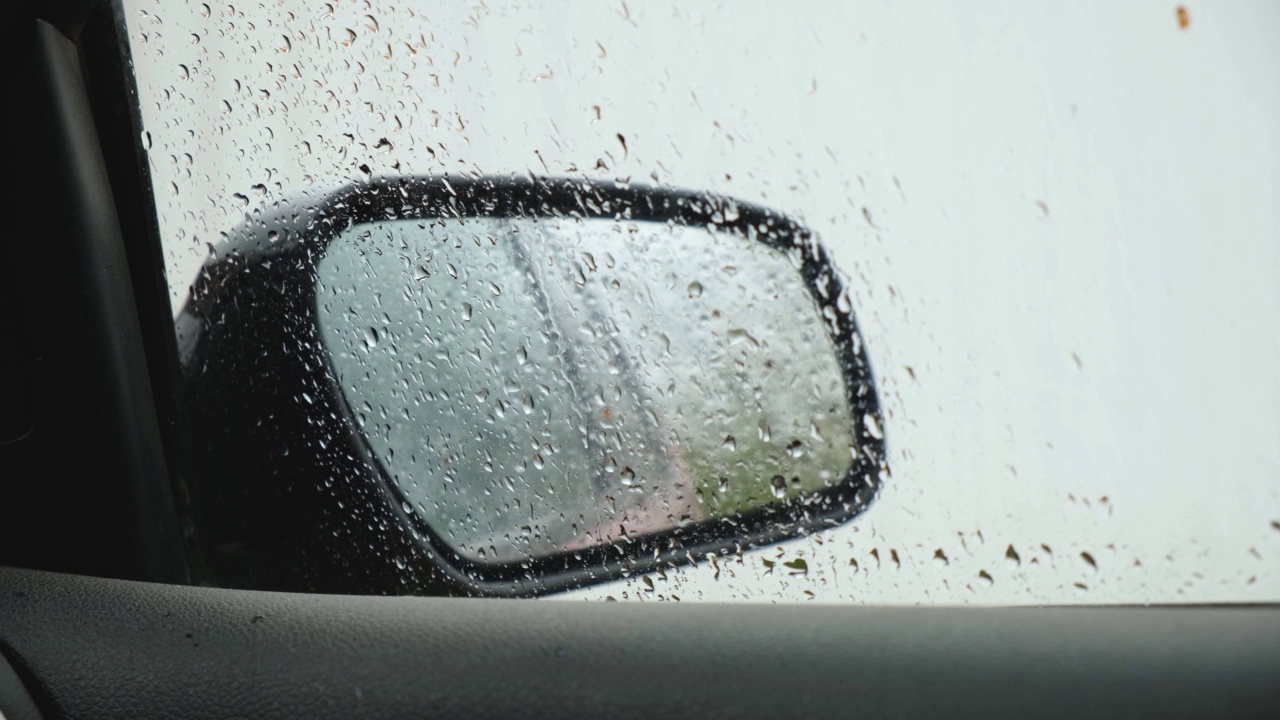 雨滴密切起来。从汽车内部的侧视镜与凝结和滴水的雨在窗户上。湿玻璃、降水。春天雨季。多云的一天。视频下载