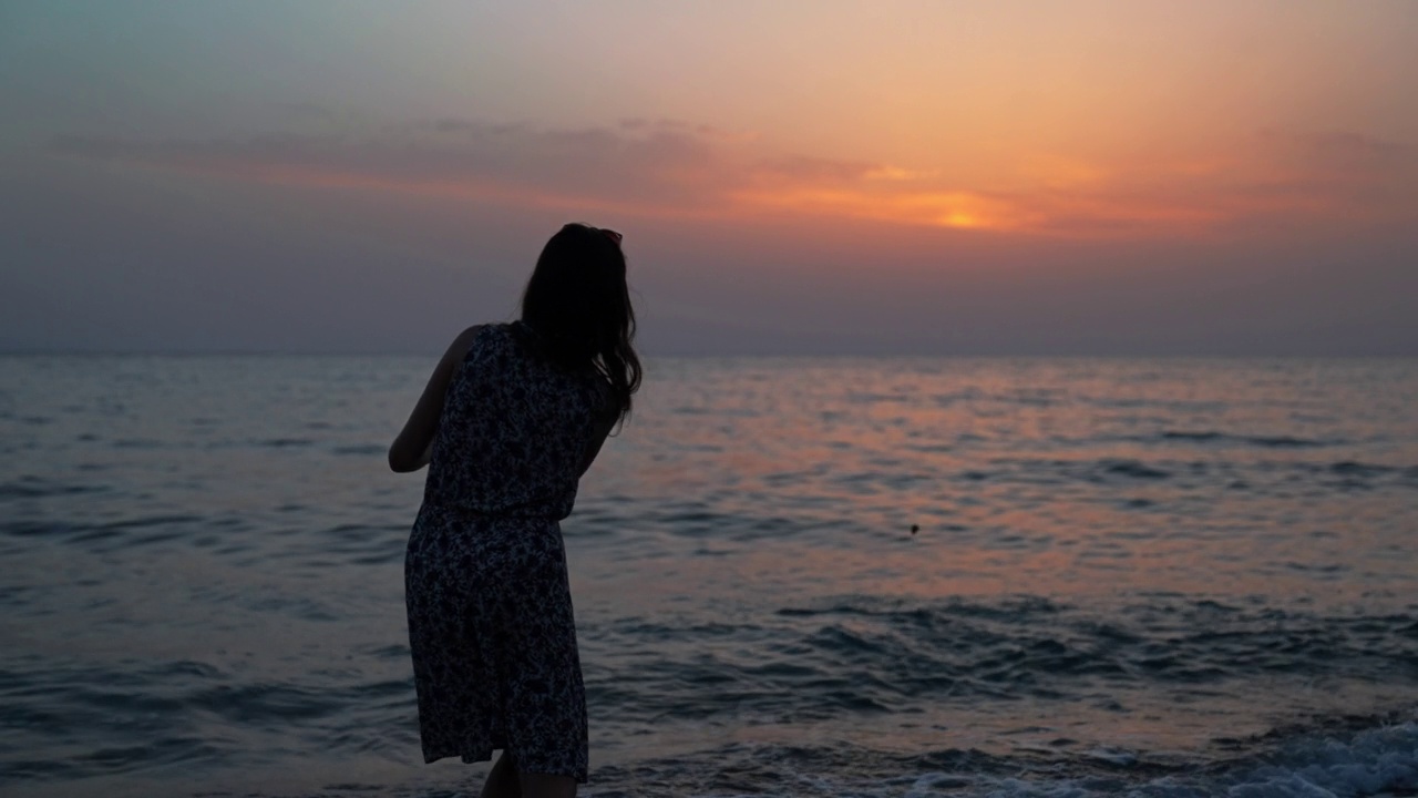 海滩上的女人剪影向海里扔石头视频素材