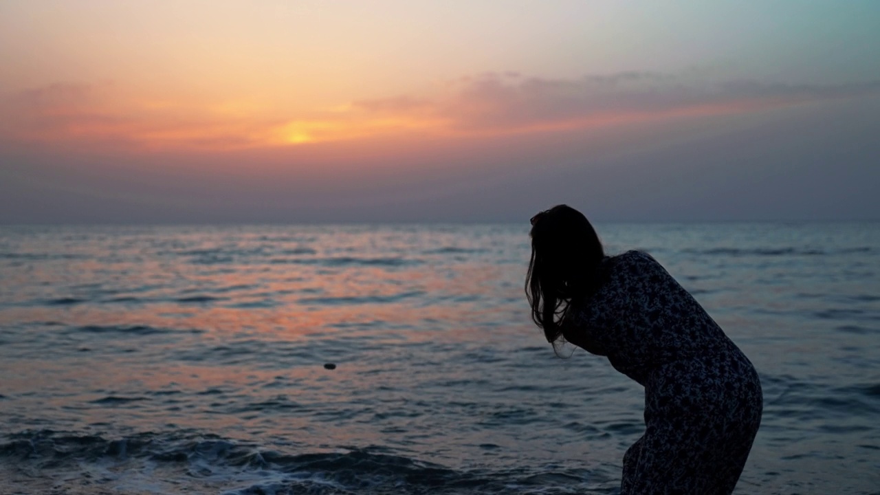 海滩上的女人剪影向海里扔石头视频素材