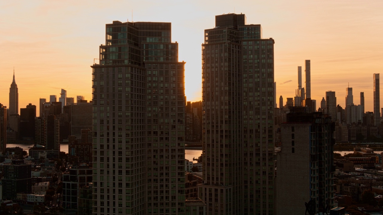 在皇后区猎人角的两座现代化塔楼之间可以看到夕阳。曼哈顿与帝国大厦隔着东河远眺。航拍视频与平移相机运动。视频素材