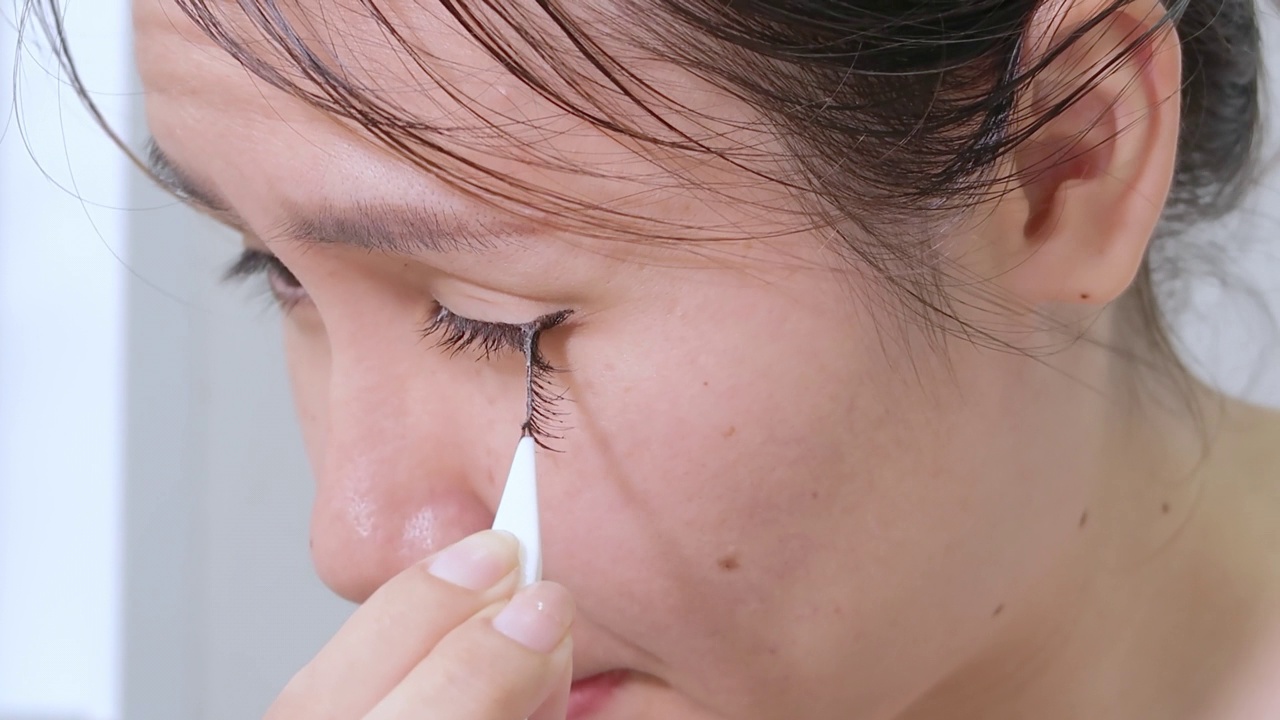 美丽的亚洲女人用钳子从她的眼睑上拔下假睫毛。视频素材