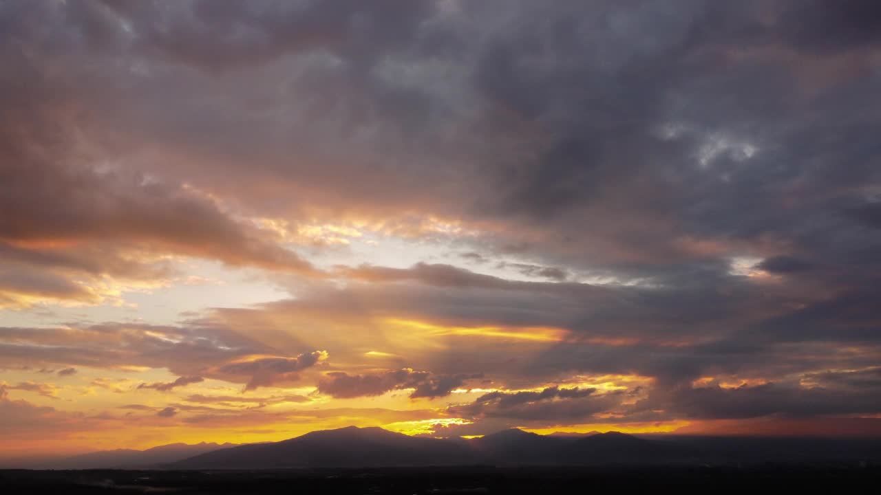 夕阳下的天空，金色的阳光映衬着山景和乡村的剪影。鸟瞰美丽的天空与云和阳光在日落。视频素材