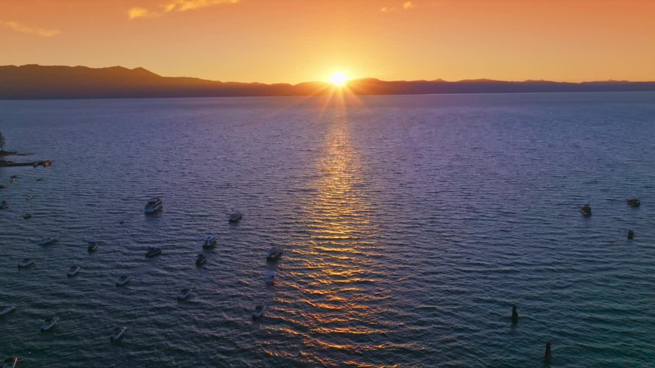 许多船只在太浩湖的水面上航行。明亮的太阳落在山的后面。背景是橙色的天空。视频素材