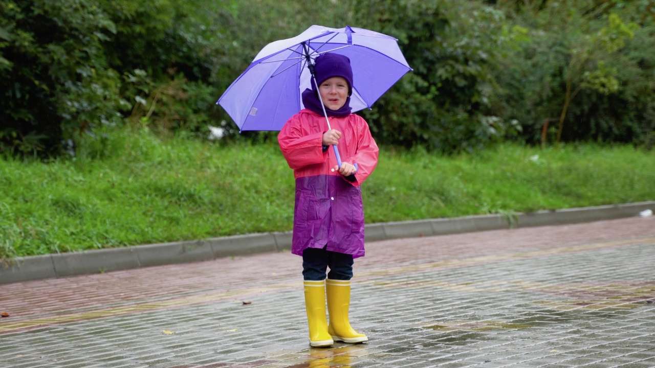 孩子在秋雨中玩耍。孩子用伞。户外乐趣的孩子，任何天气。防雨服，儿童用靴子和夹克。视频素材