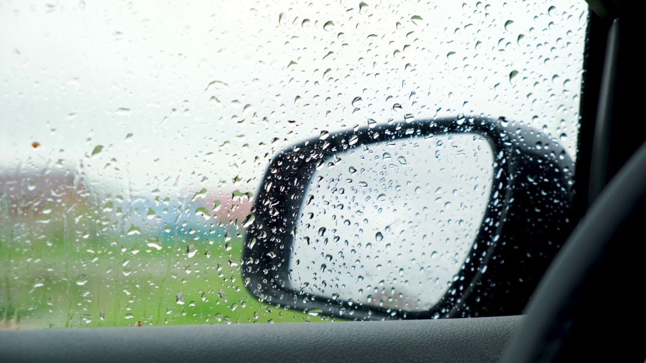 雨滴密切起来。从汽车内部的侧视镜与凝结和滴水的雨在窗户上。湿玻璃、降水。春天雨季。多云的一天。视频素材